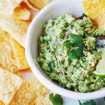a bowl of guacamole with tortilla chips on the side.