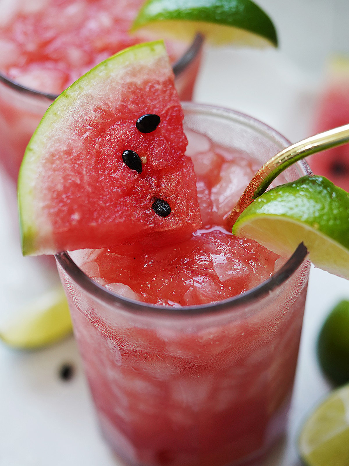 A tall glass with watermelon drink topped with a watermelon slice.