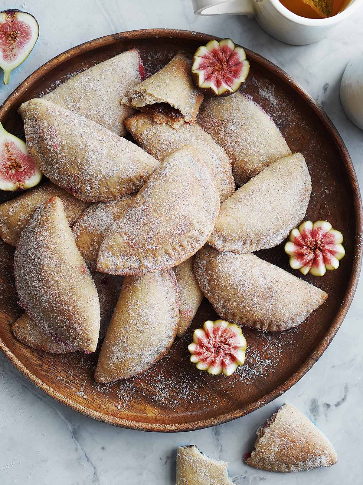 Sweet Empanadas on a serving tray with cut figs on the side.