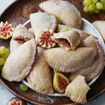 Crispy sweet empanadas on a white plate placed on a wood serving tray.