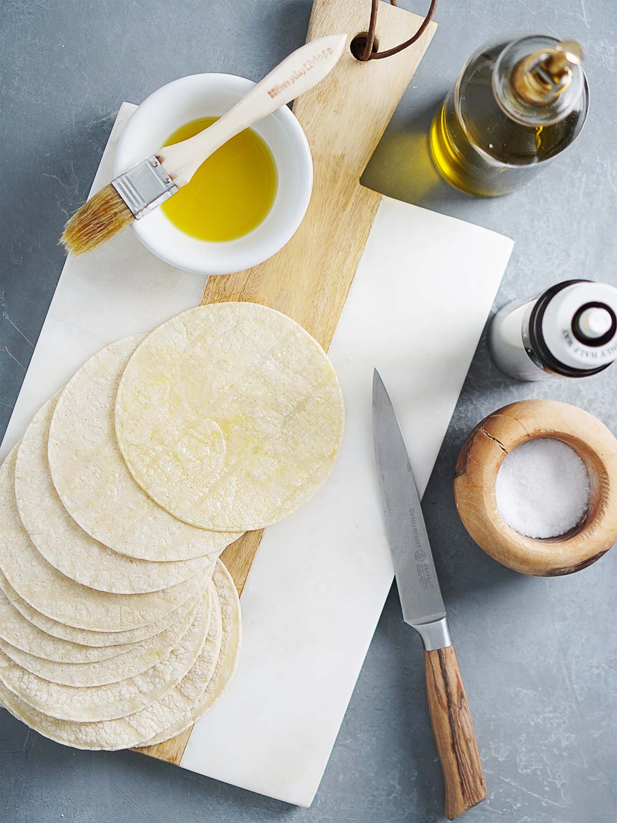Corn tortillas placed on a cutting board with a small bowl of oil on the side.