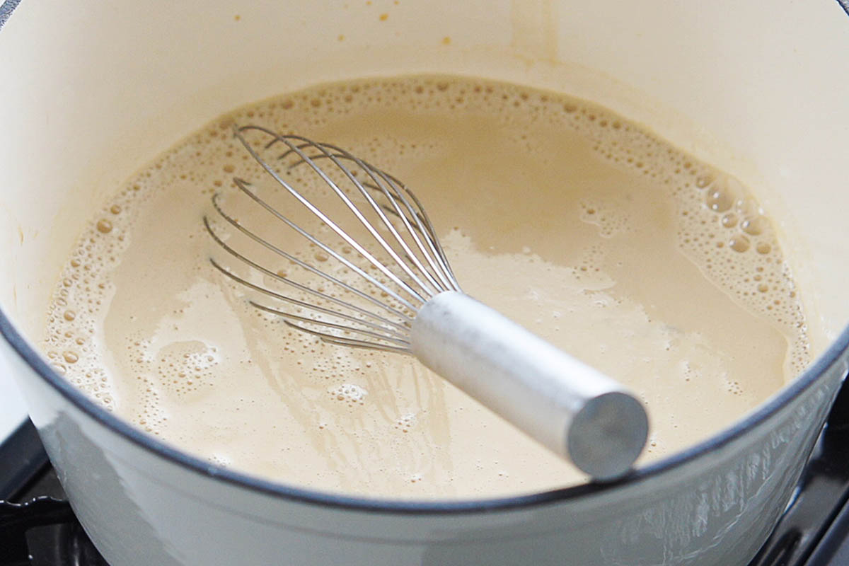 Milk being whisked in a gray saucepan.