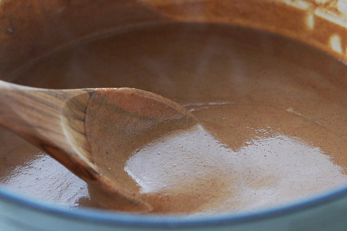 A saucepan with champurrado and a wood spoon.
