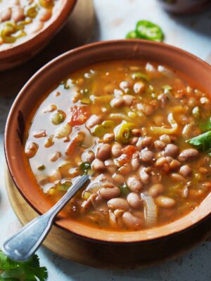 A brown bowl with beans and a spoon.