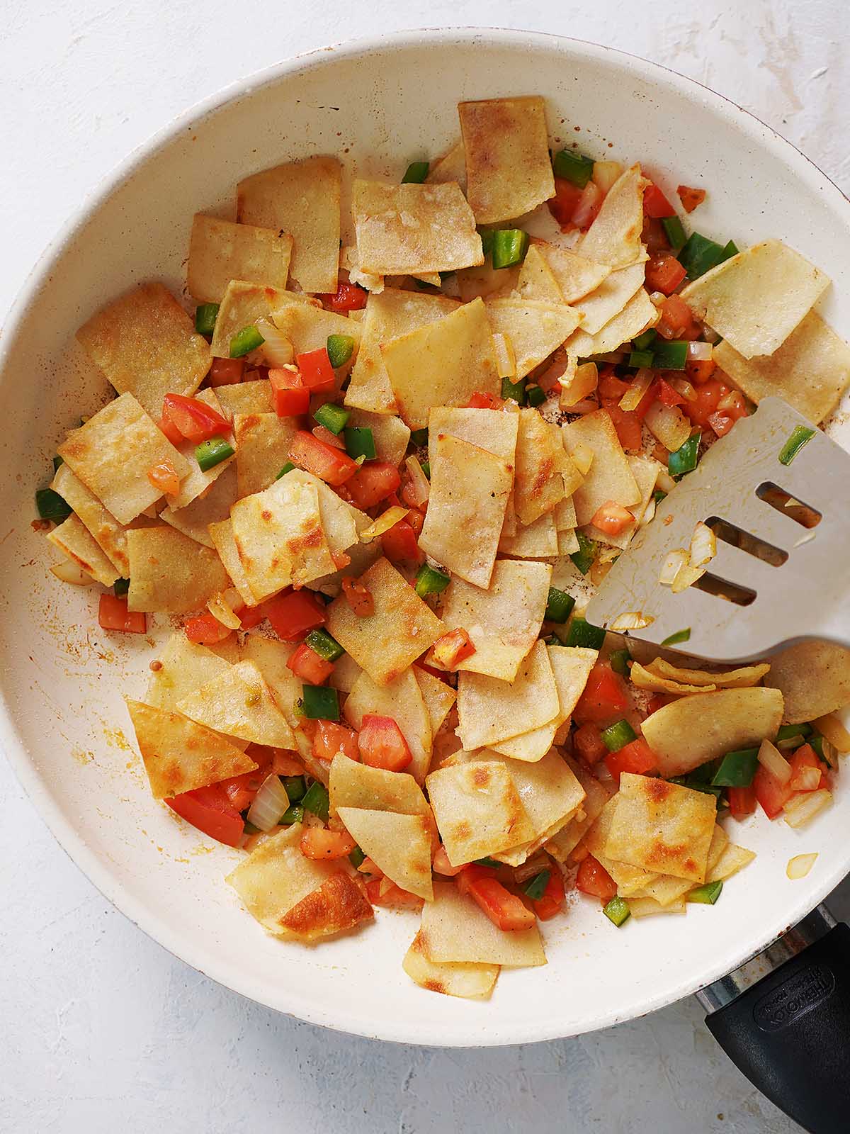 Frying corn tortillas, onions, jalapeños and tomatoes on a skillet.