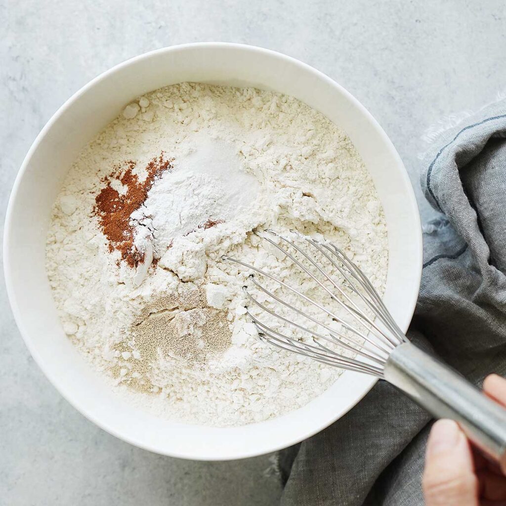 Mixing flour and cinnamon with a whisk on a white bowl.