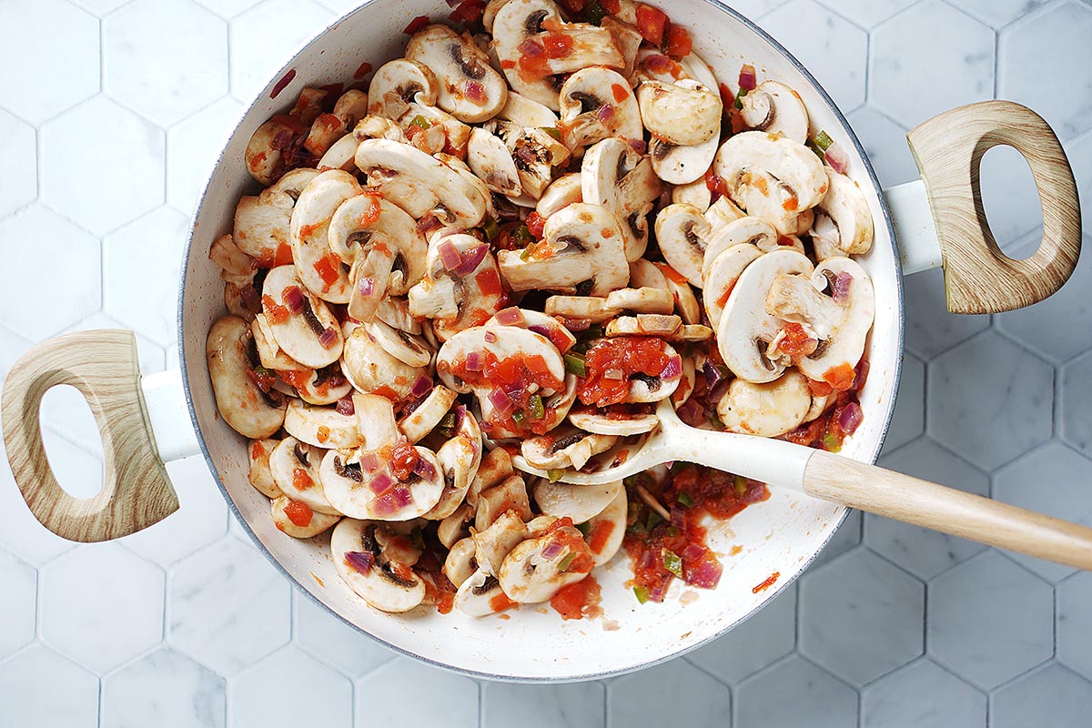 Sauteing mushrooms with tomatoes in a large skillet.