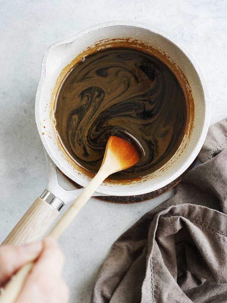 A small saucepan with melted syrup in it and a cooking wooden spoon.