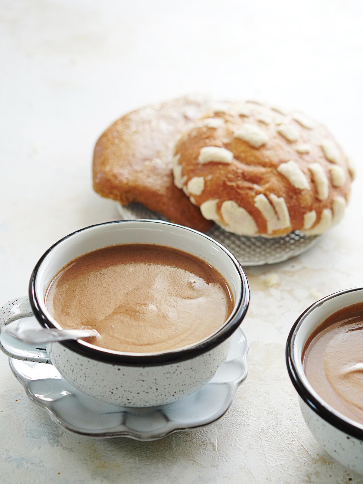 Two cups with Champurrado and pan dulce on the side.