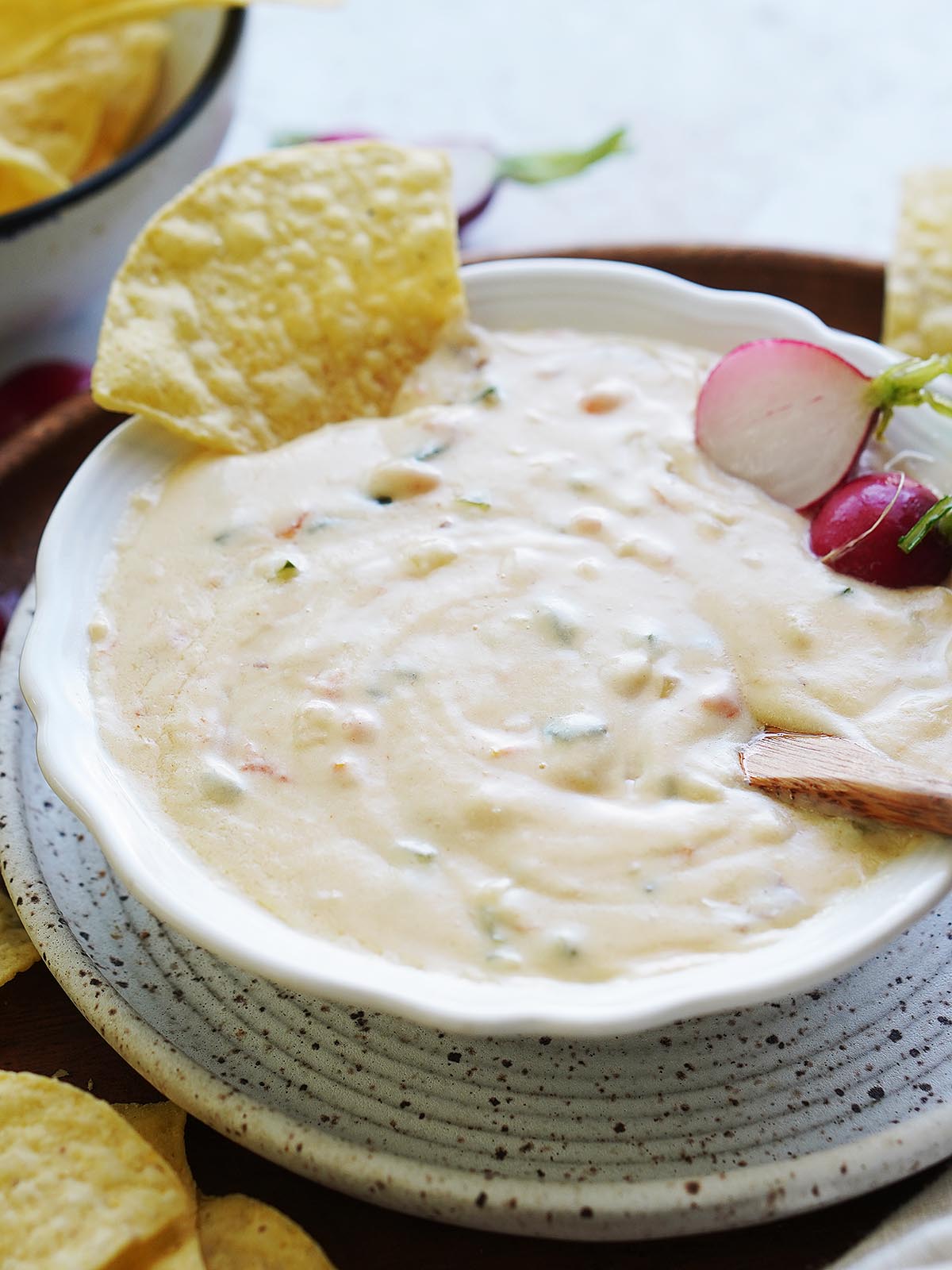 Queso dip in a white bowl with tortilla chips on the side.