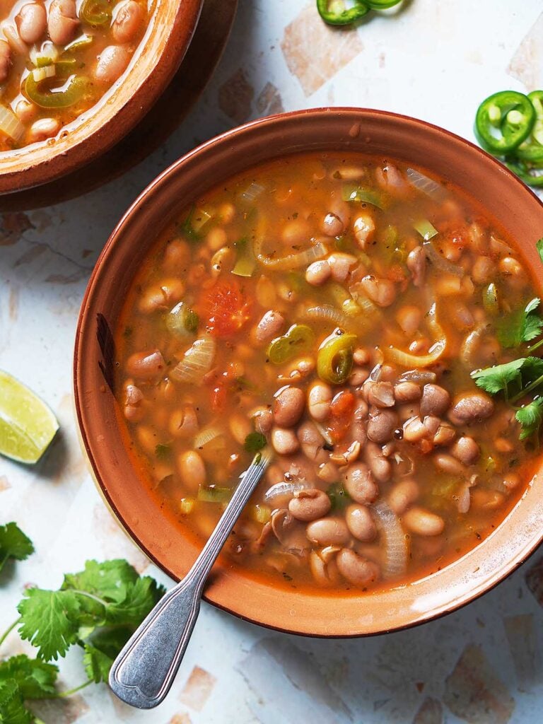 A brown bowl with charro beans and a spoon.