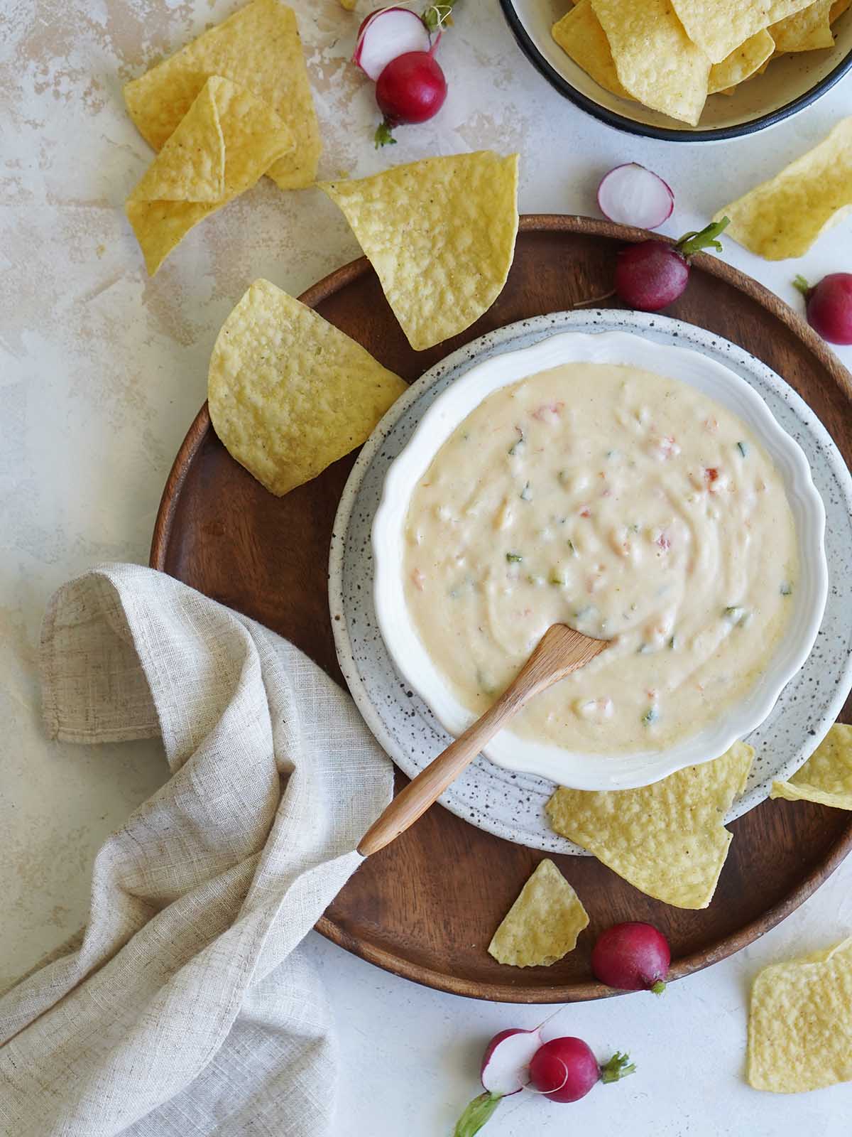 A bowl of white queso dip placed on a wooden plate.