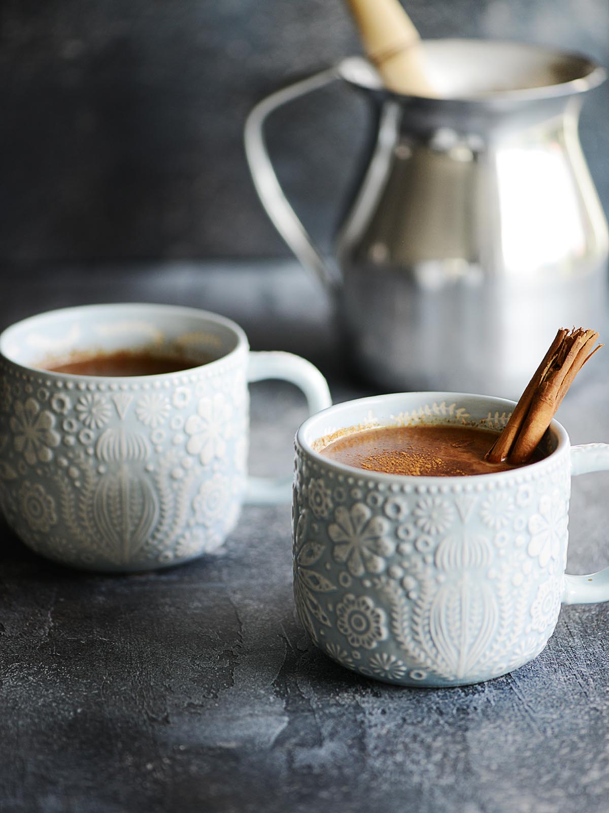 Two blue mugs with chocolate and a cinnamon stick. 