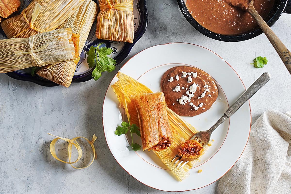 A plate with one tamales with beans on the side.
