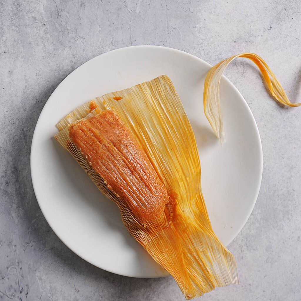 A plate with a tamal half unwrapped from the husk.