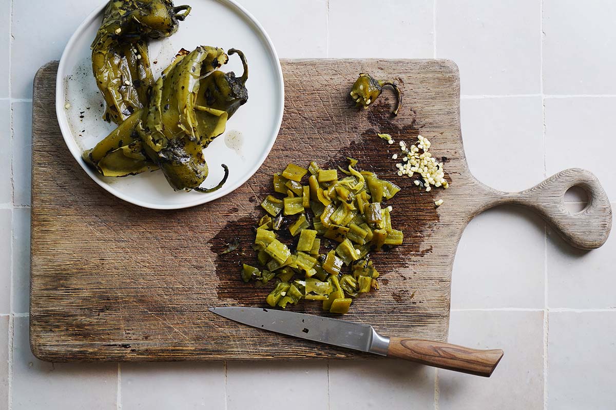 Chopping roasted green chiles on a cutting board.
