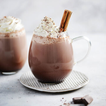 Two clear mugs with hot chocolate and whipped cream.