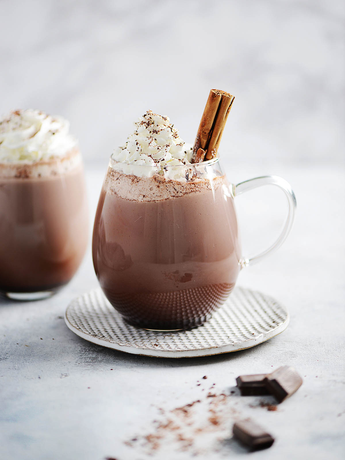 Two clear mugs with hot chocolate and whipped cream.