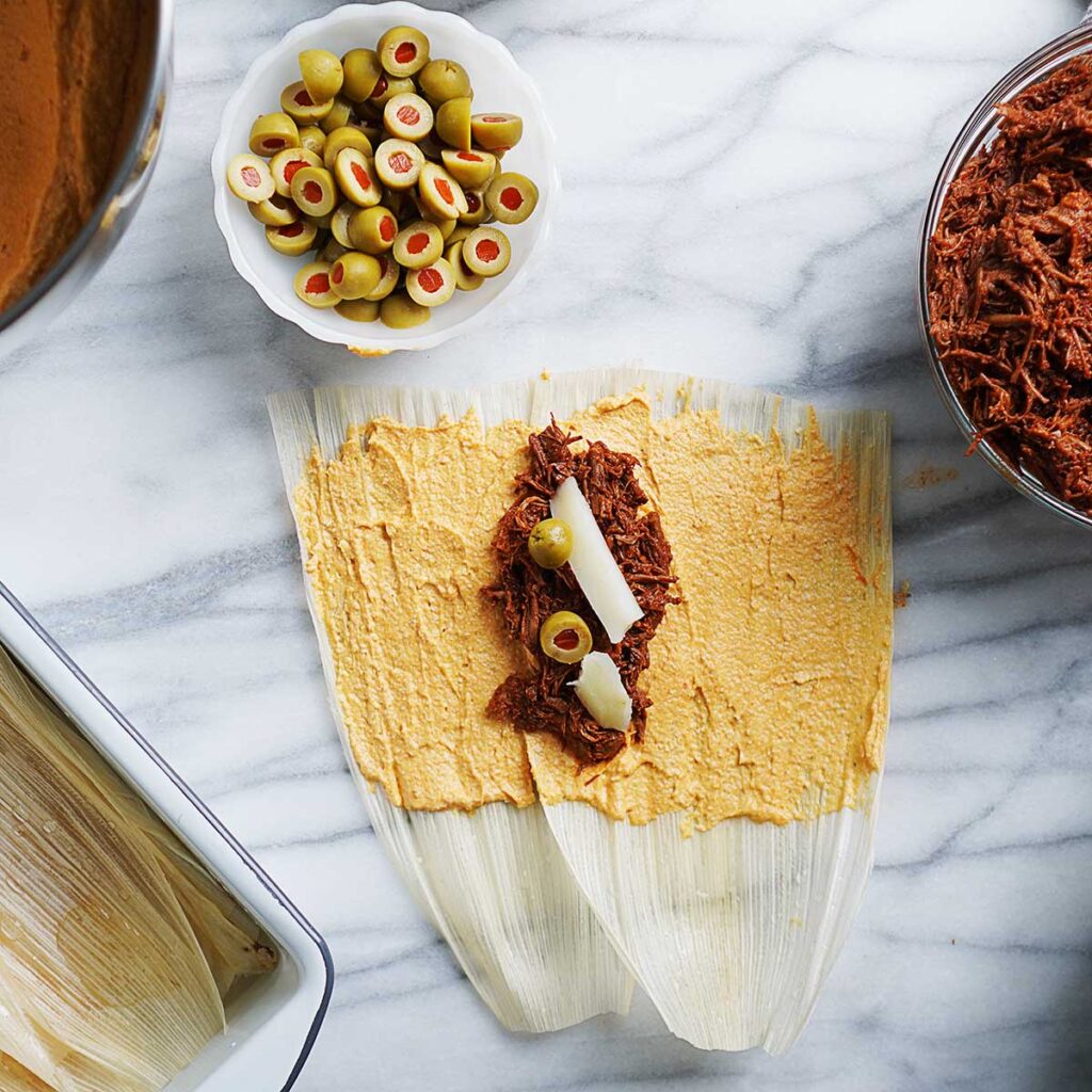 Filling a tamal with shredded beef, potato slices & olives.