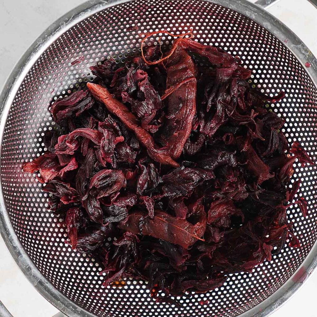 A strainer with cooked jamaica flowers and tamarindo pods.