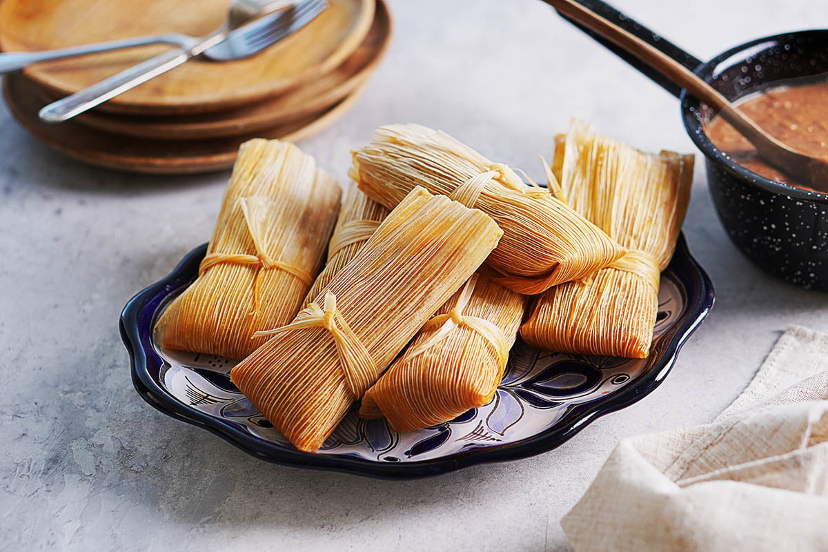 A few tamales on a blue oval plate with serving plates on the side.