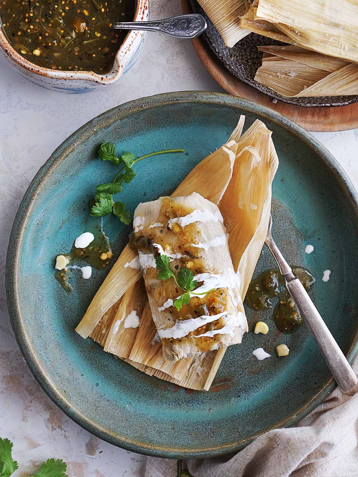 A green chile corn tamal placed on husks on a green plate.