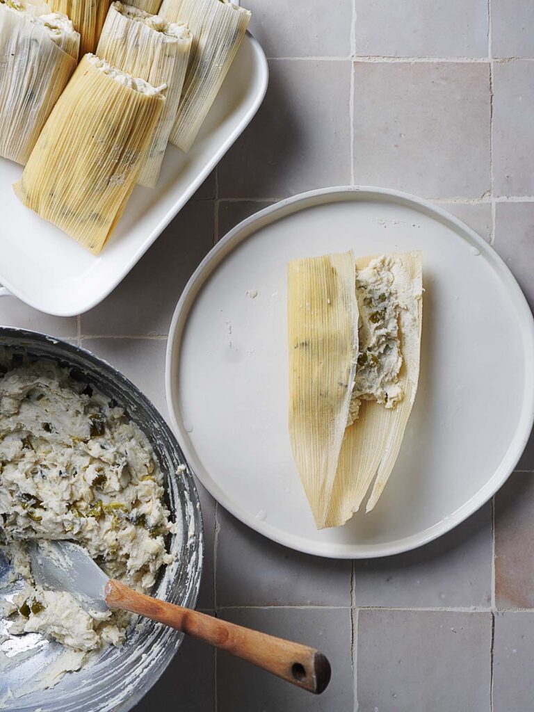 Folding a tamal with corn husk placed on a plate.