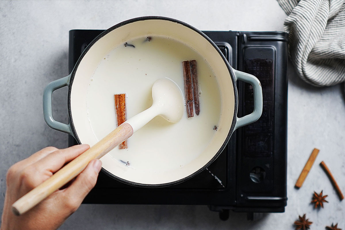 Stirring a pot with milk, cinnamon sticks and cloves.