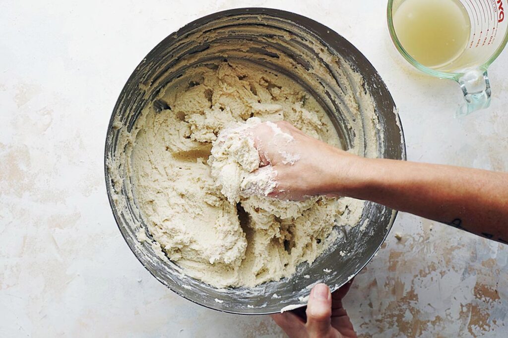 Mixing dough with one hand in a large bowl.