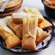A few tamales on a blue oval plate with serving plates on the side.
