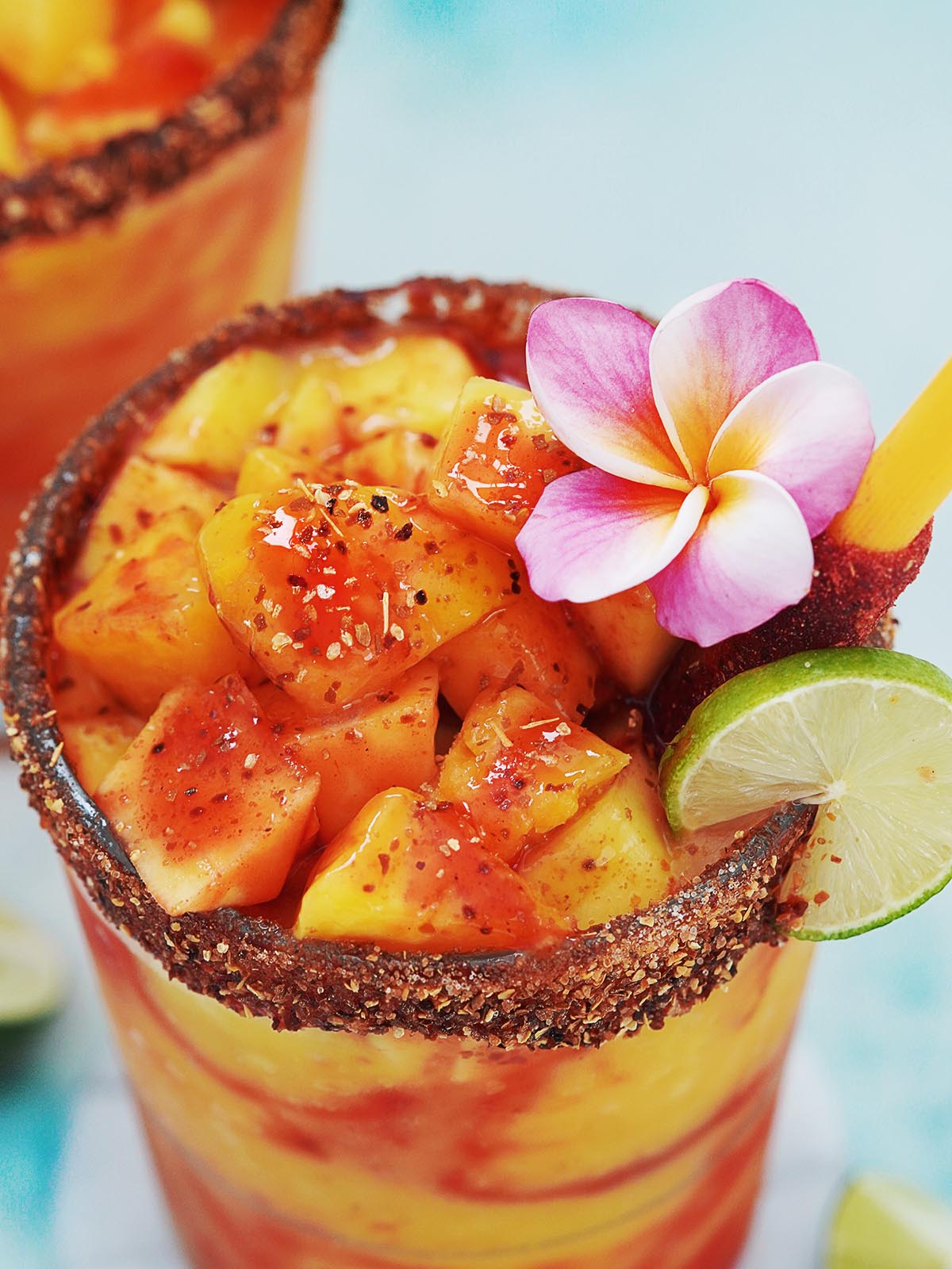 A close up image of a mangonada cup garnished with mango chunks and a slice of lime.