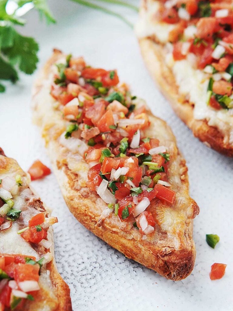 Three molletes on a white plate topped with salsa fresca.