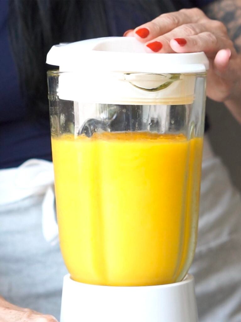 Blending frozen mango with mango juice and ice in a blender.
