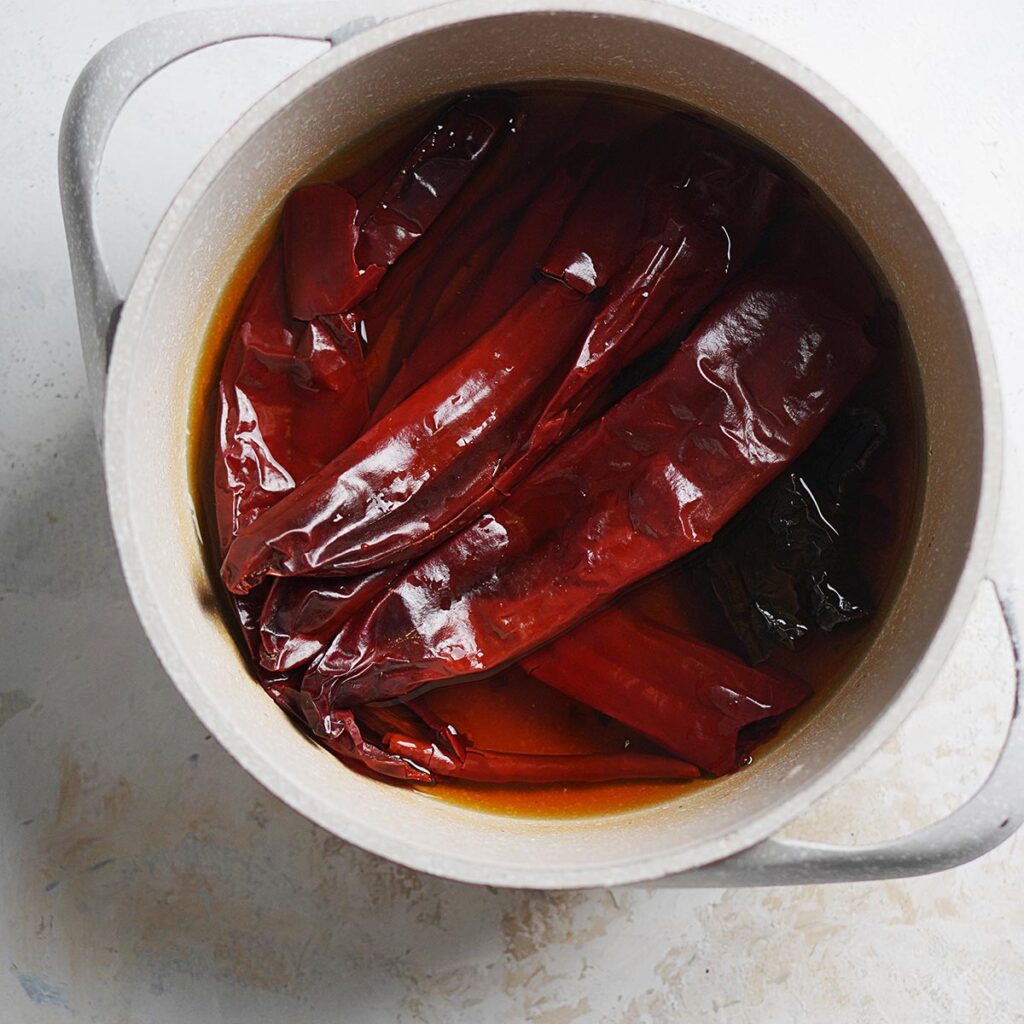A small pot with dried chiles in water.