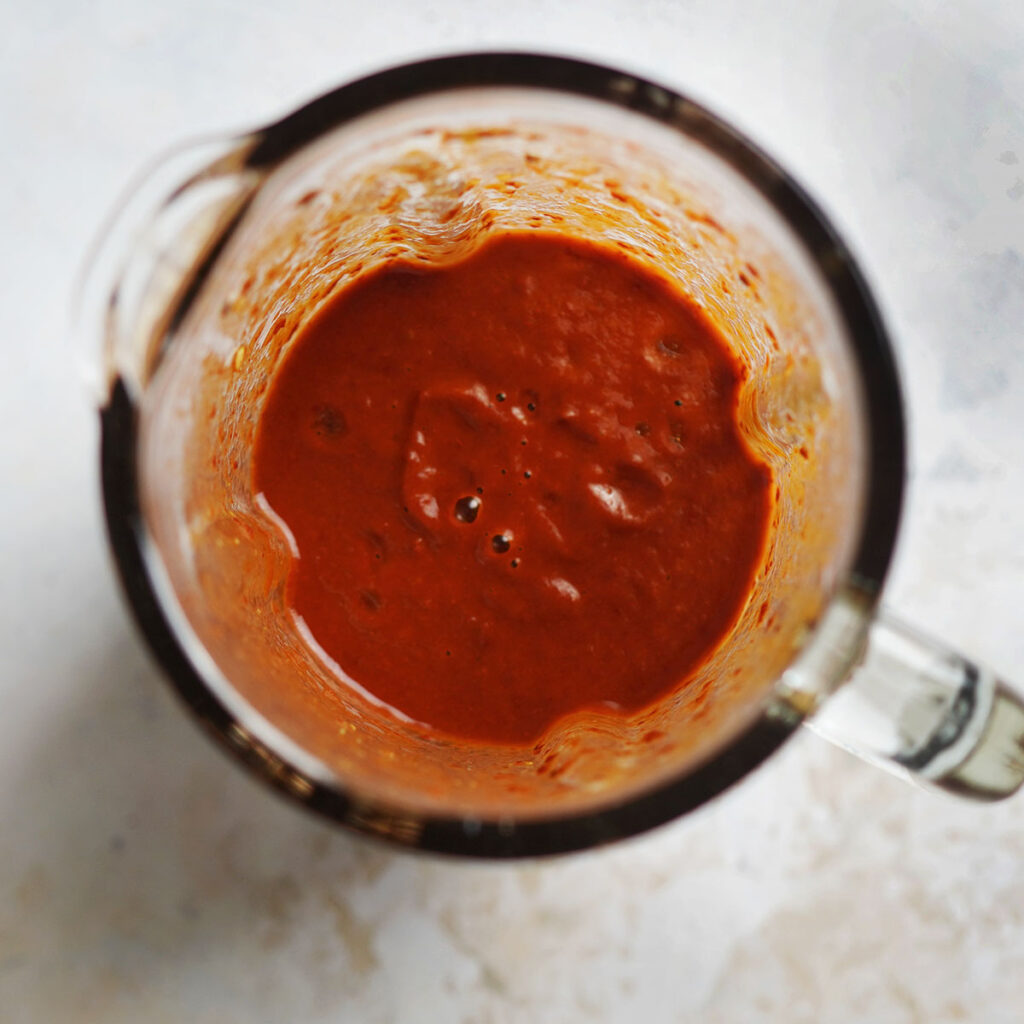 A blender cup with red chile sauce.