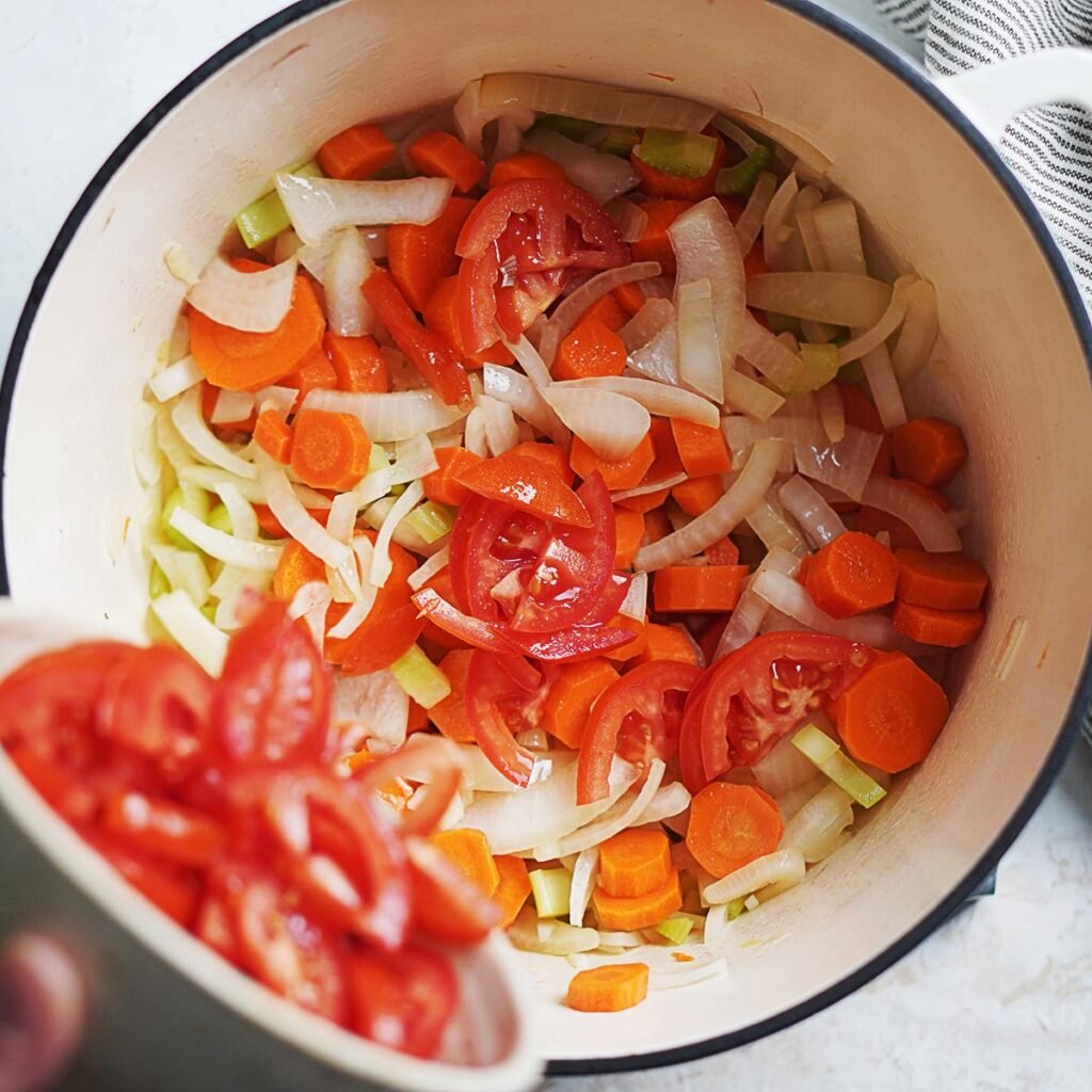Sauteing carrots, celery, tomatoes and onions in a large pot.