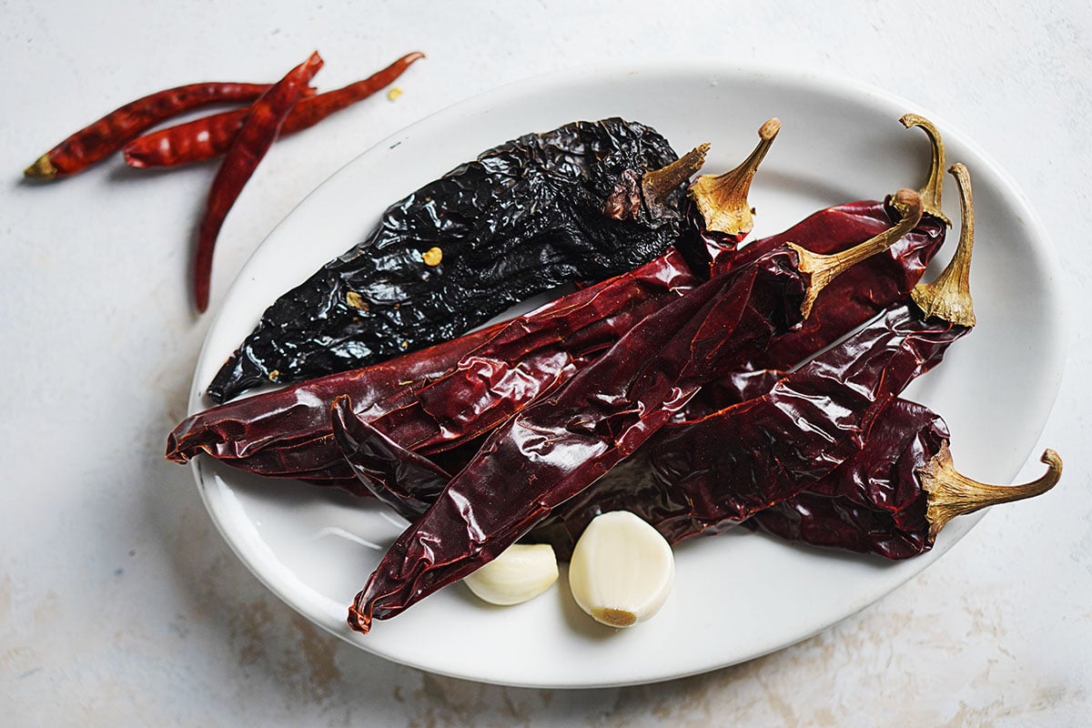 An oval plate with dried chiles and garlic cloves.