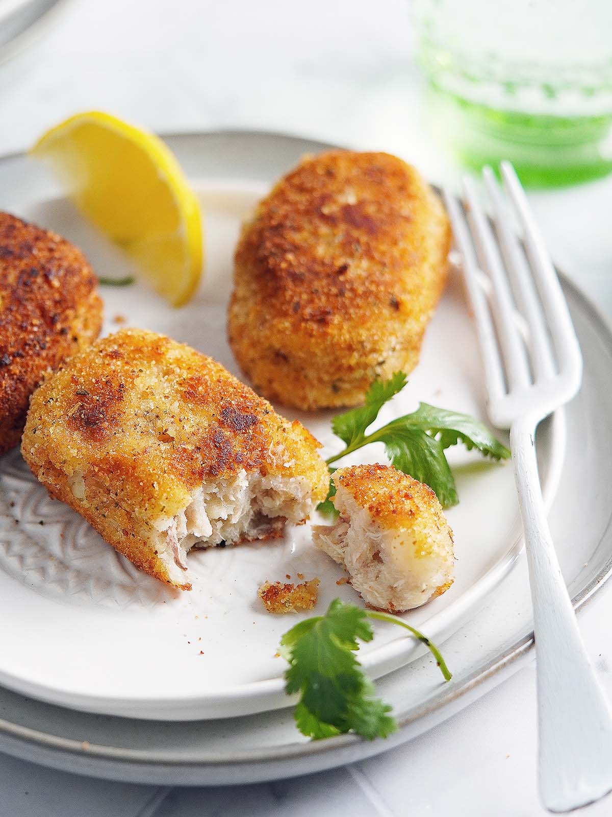 3 croquetas de atun on a white plate with a lemon on the side.
