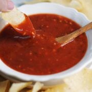 A hand holding a tortilla chip and dipping it into salsa.