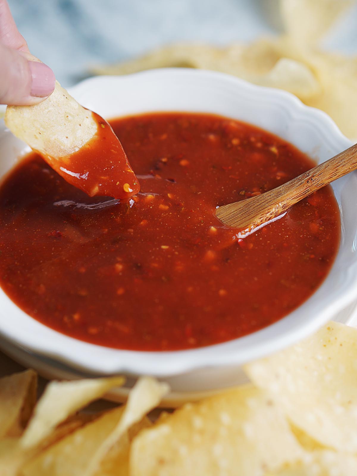 A hand holding a tortilla chip and dipping it into red sauce.