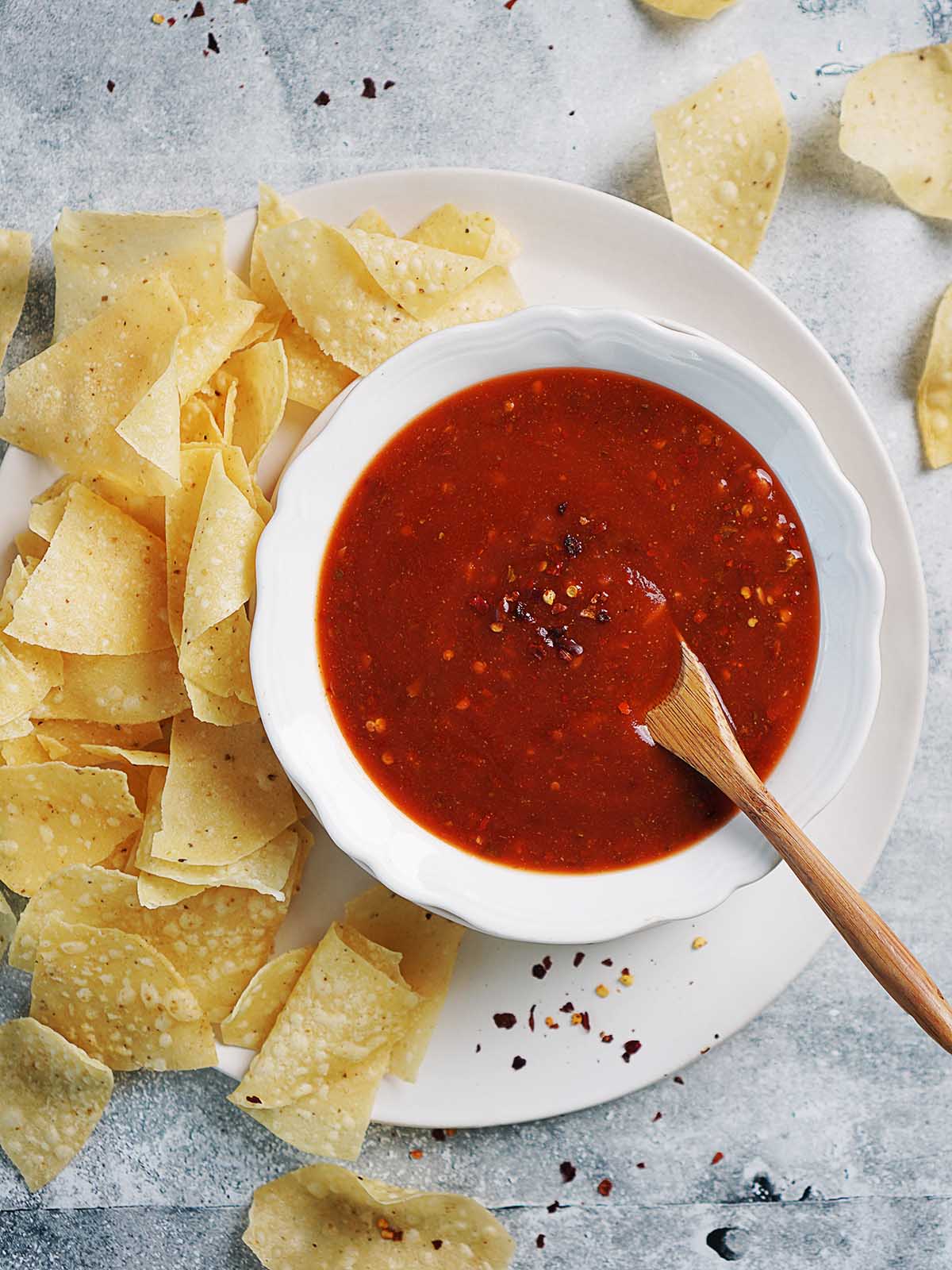 A bowl with red sauce and tortilla chips on the side.