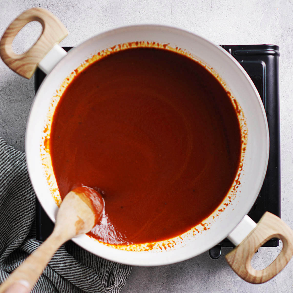A pan with enchilada sauce and a wooden spoon.