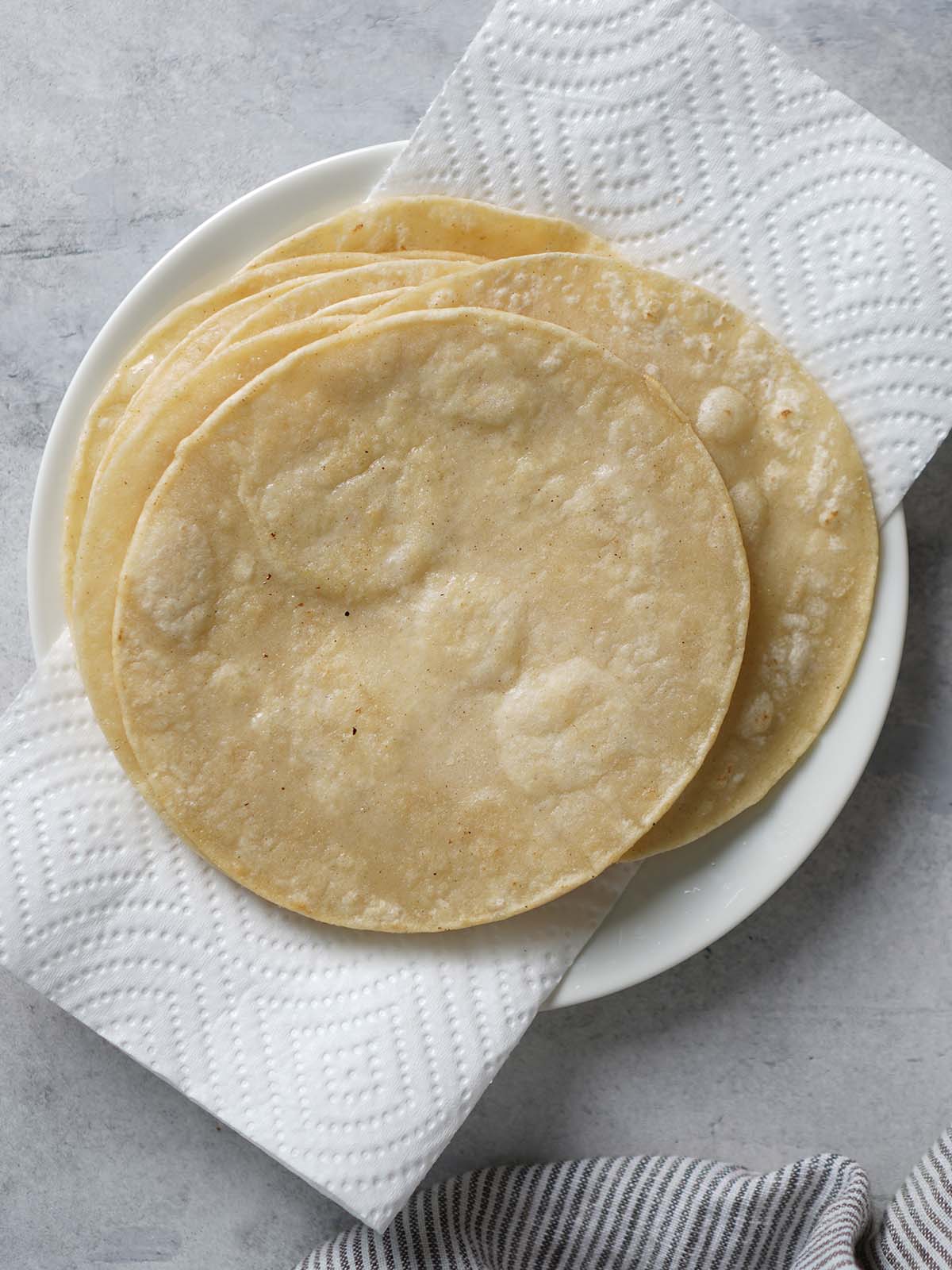 A stacked of fried corn tortillas placed on a paper towel on a plate.