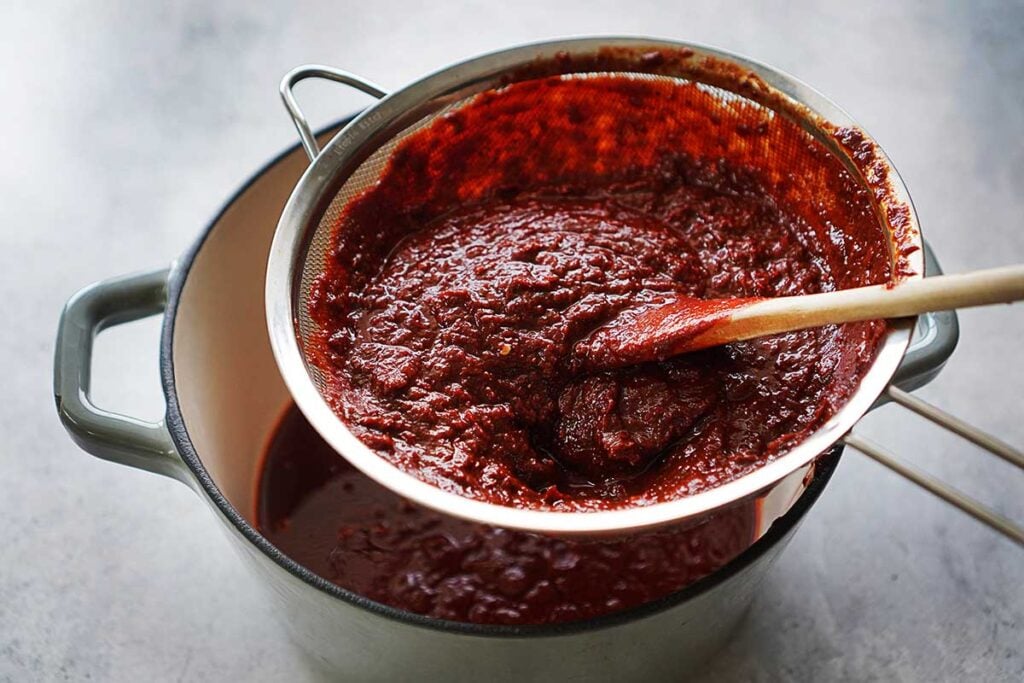 Straining red sauce thru a colander into a pot.