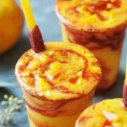 3 plastic cups with cold mango drink topped with mango cubes.