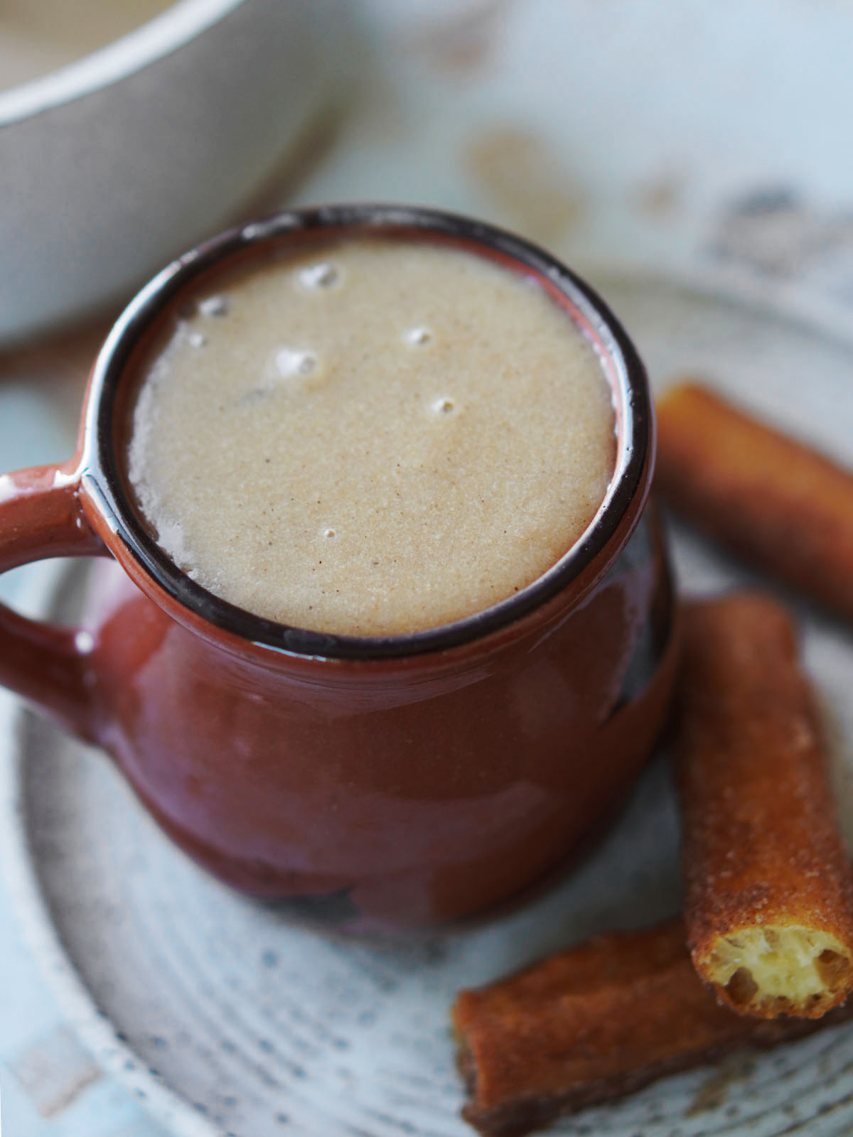 A ceramic cup with Atole and churros on the side.