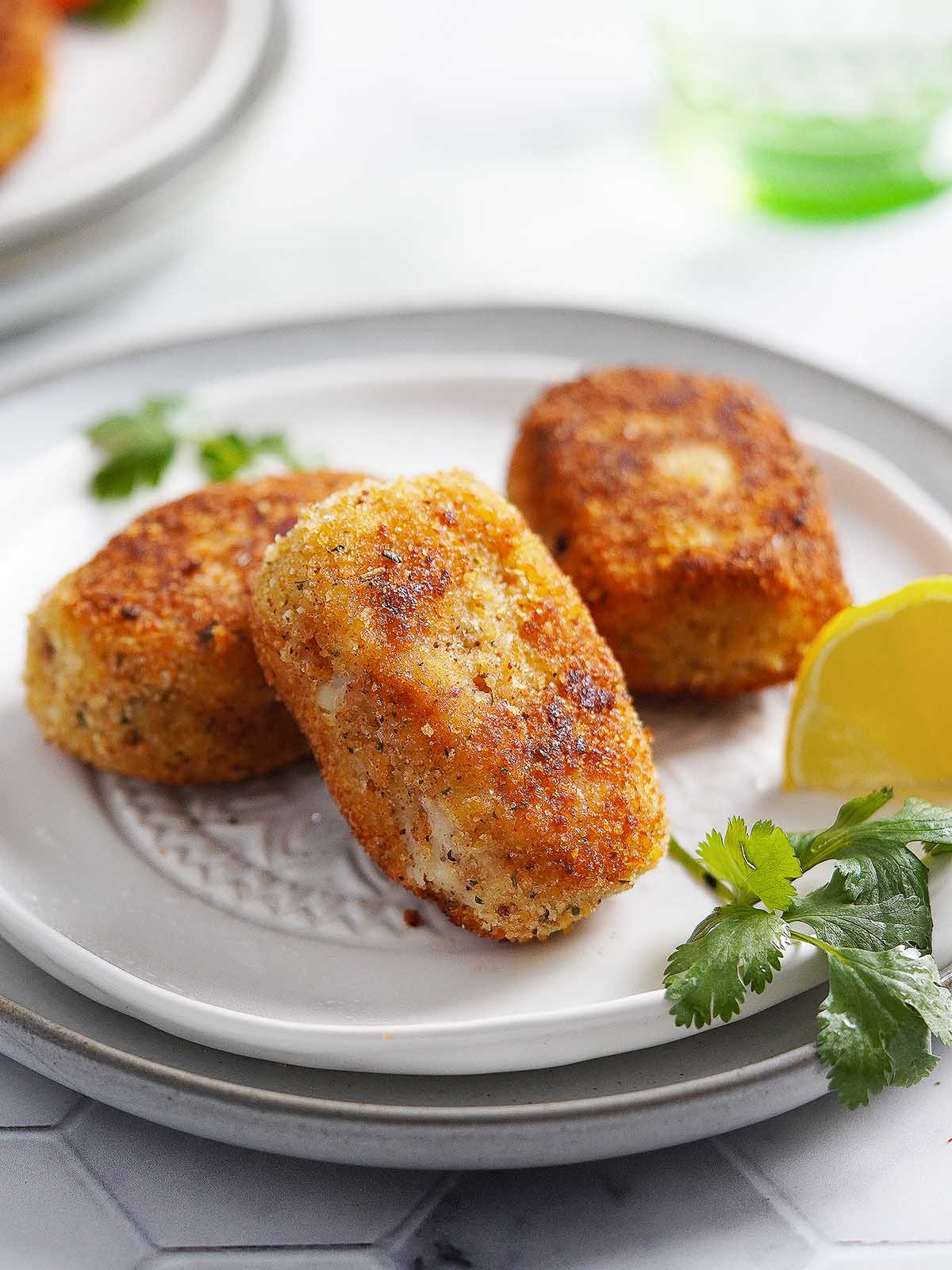 3 croquetas de atun on a white plate with a lemon on the side.