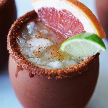 A clay cup with a cocktail garnished with a slice of grapefruit.