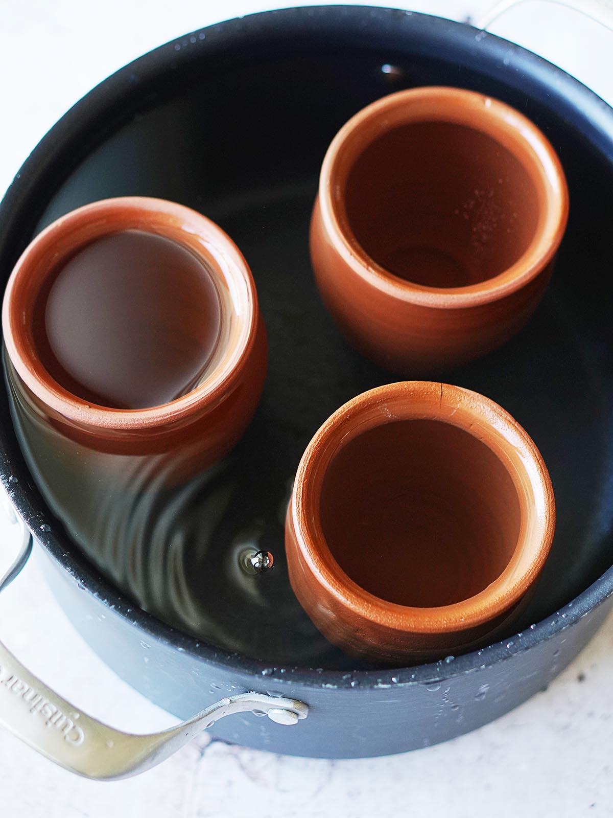 A large pot with the clay cups placed in there filled with water.