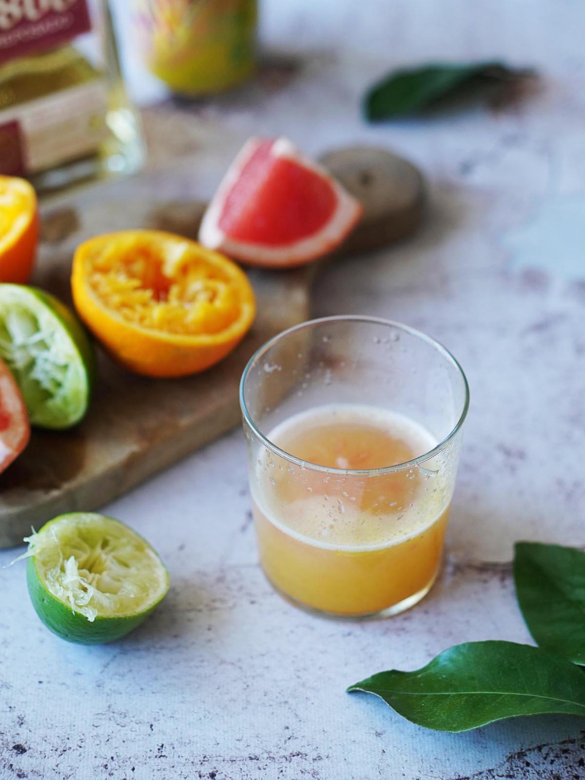 A glass with citrus juice plus squeezed oranges and grapefruits next to it.